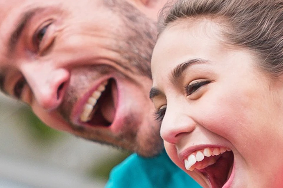 Two people smiling while riding a blue alpine coaster on a track surrounded by greenery.