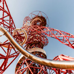 Röd gitterstruktur med sammanflätade silverglas, mot en klarblå himmel.