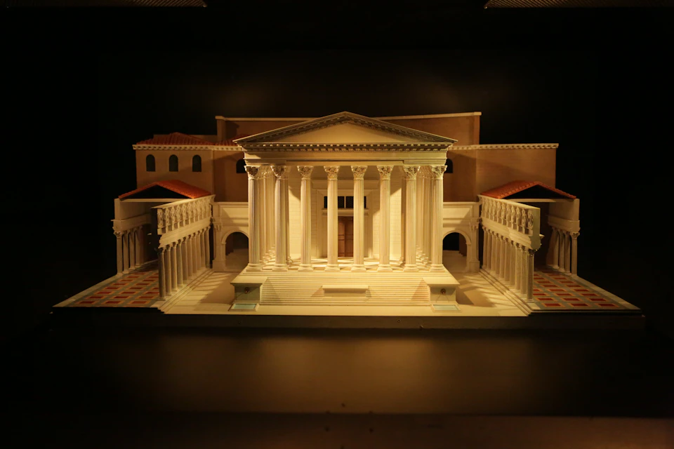 A detailed miniature model of an ancient Roman-style building with columns and red-roofed structures around it.