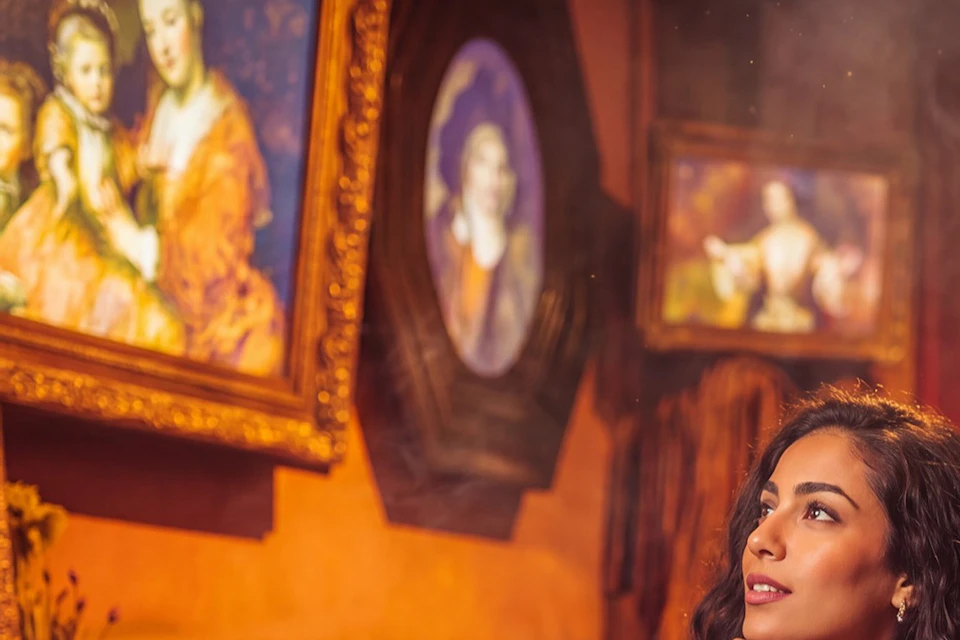 A woman and a man admire framed paintings in a warmly lit gallery.