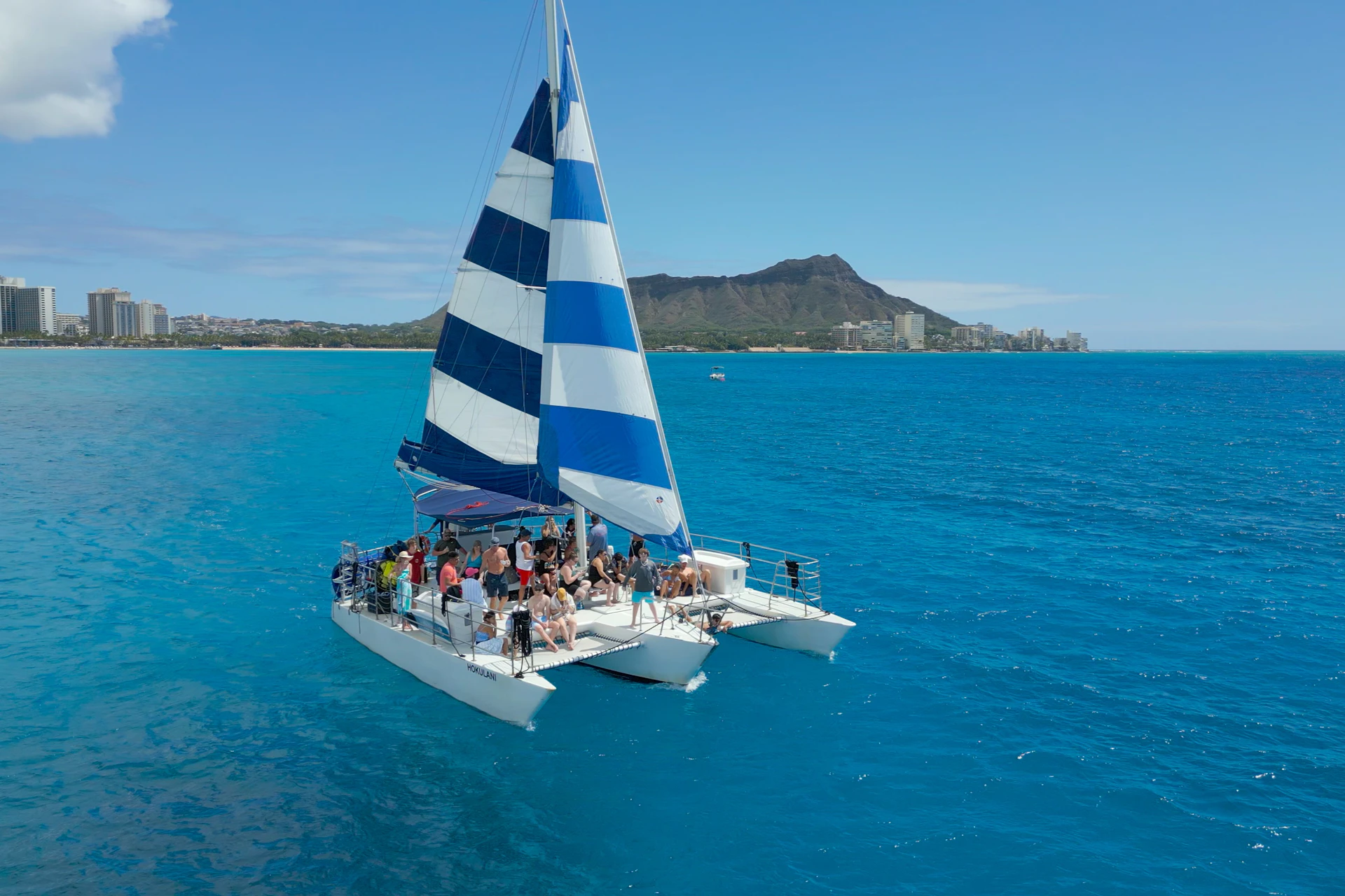 Sailing catamaran Hokulani with guests aboard, cruising off Waikiki with Diamond Head in the background.
