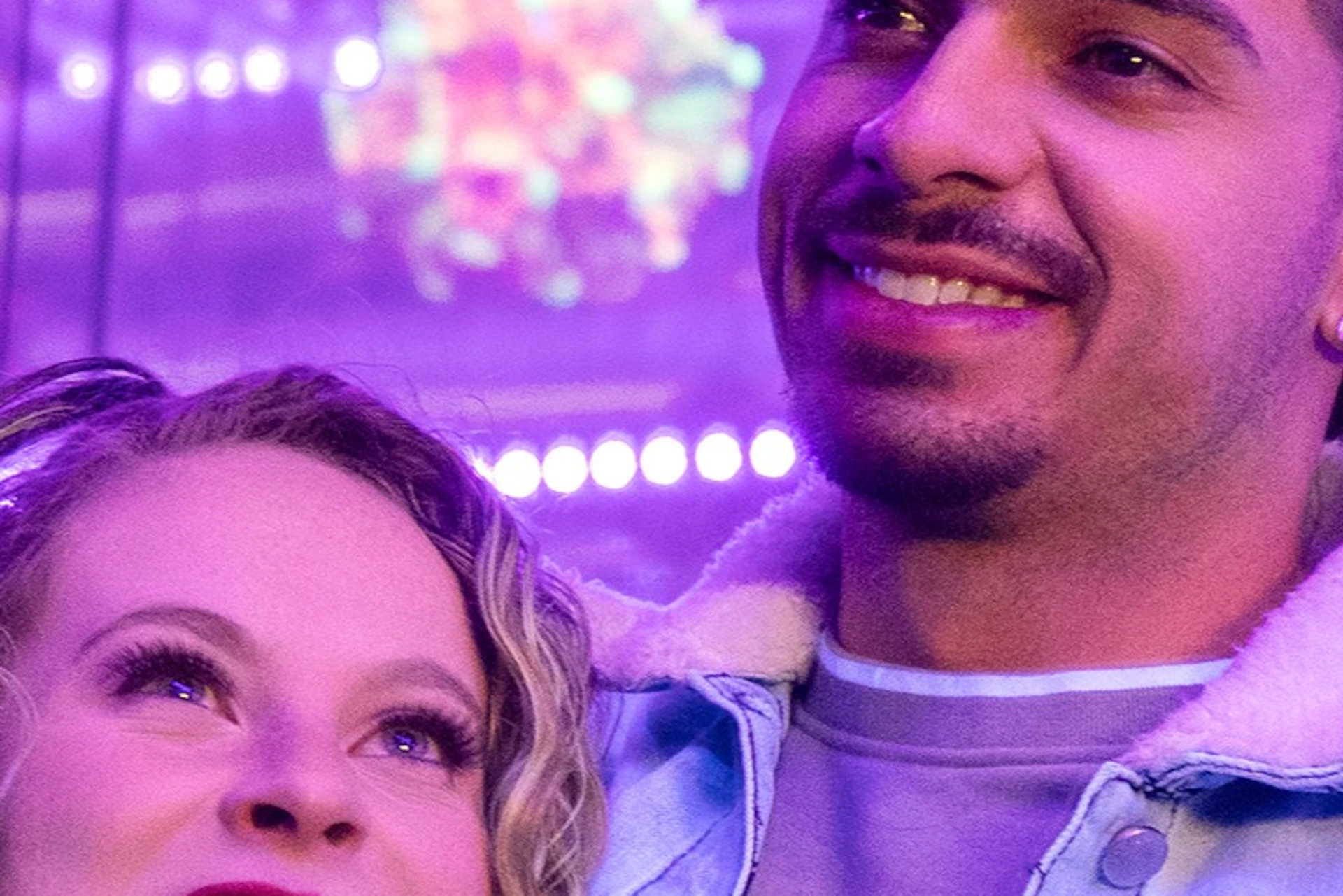 Two people smiling and posing together in a vibrant, neon-lit setting with colorful decorations in the background.