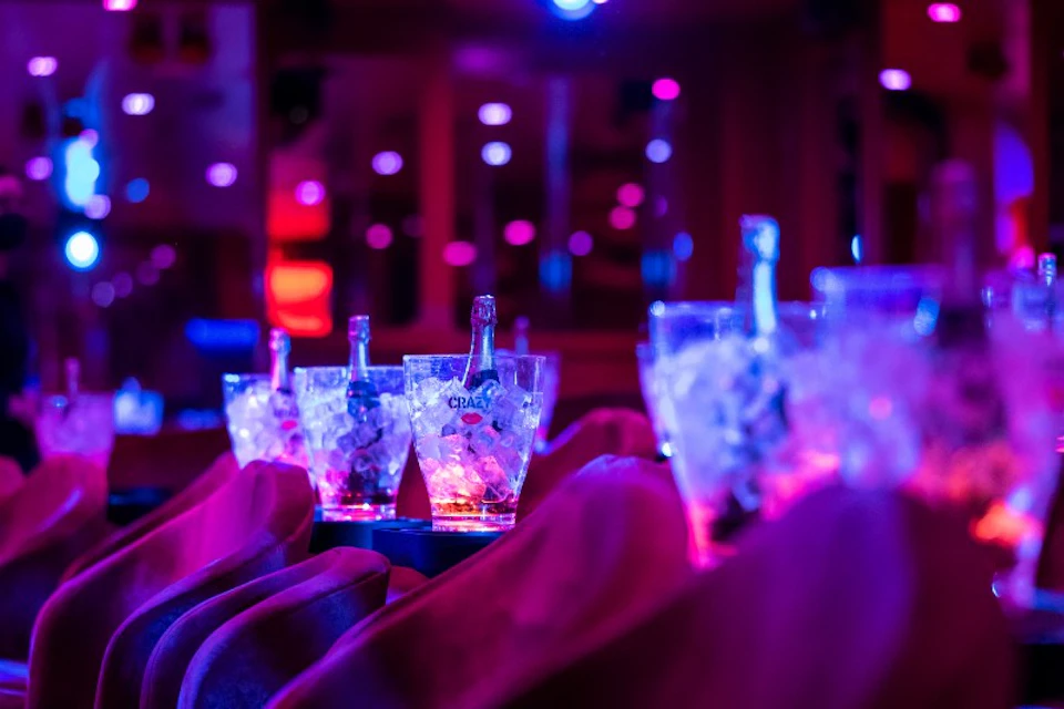 Rows of red theater seats with ice buckets containing bottles of champagne under purple and blue ambient lighting.