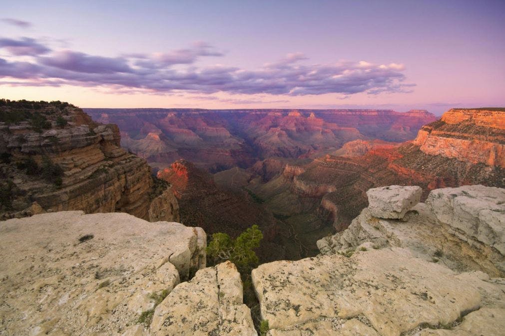 View of the Grand Canyon at sunrise with rugged, layered rock formations and a few scattered clouds in the sky.