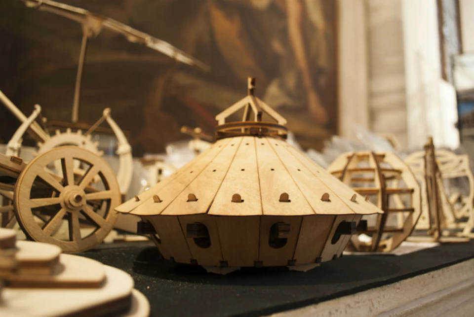 Wooden model of a dome-shaped structure with small cut-outs, surrounded by other similar wooden models in a workshop setting.