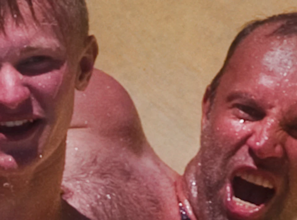 Two men on a yellow inflatable raft sliding down a water slide, with water splashing around them.