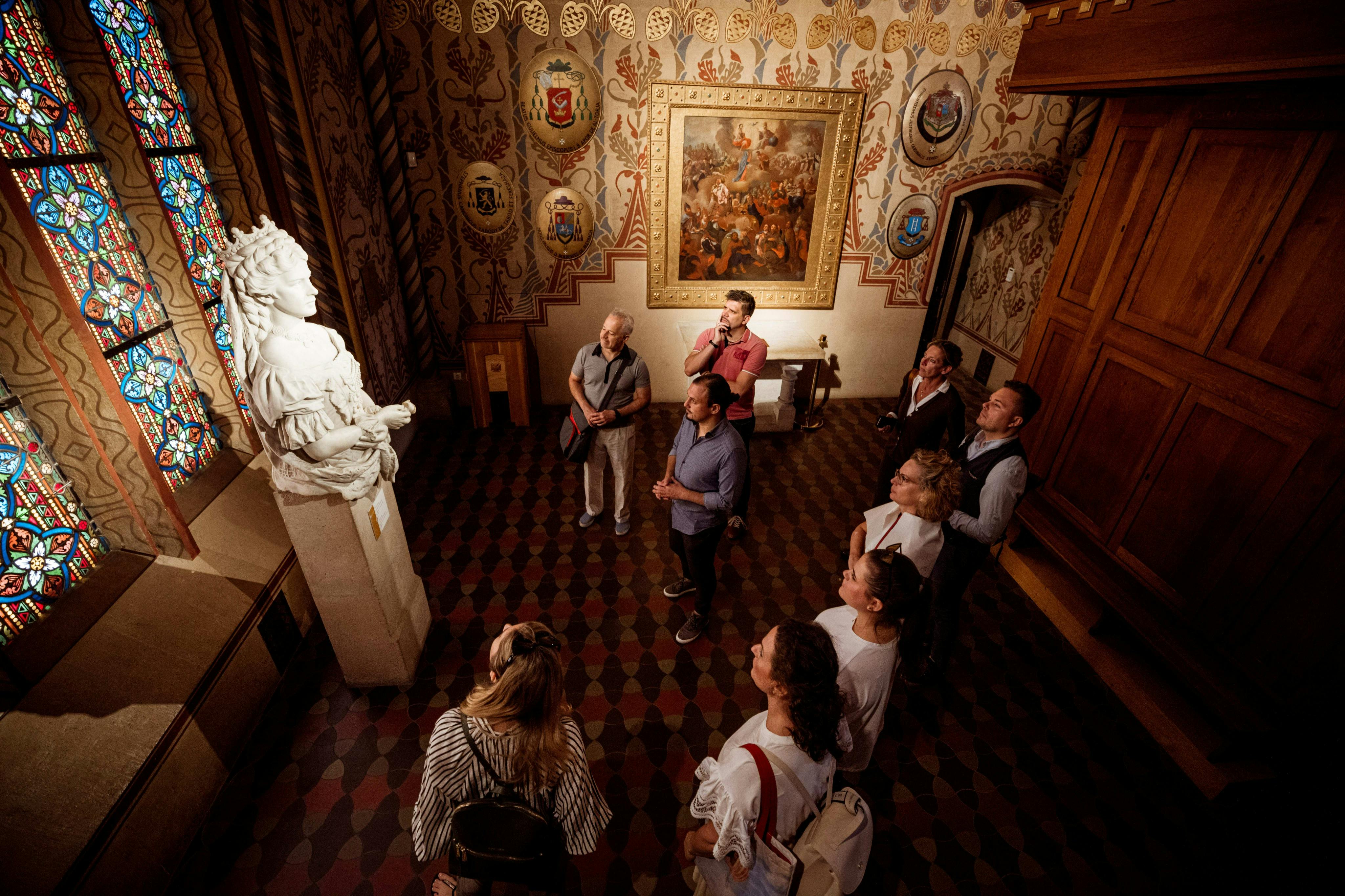 A group of people in a richly decorated room, observing artwork on the walls and a statue.