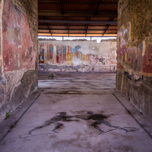 Forntida ruiner med blekta väggmålningar, en mosaik av två figurer på golvet och ett trätak ovanför.
