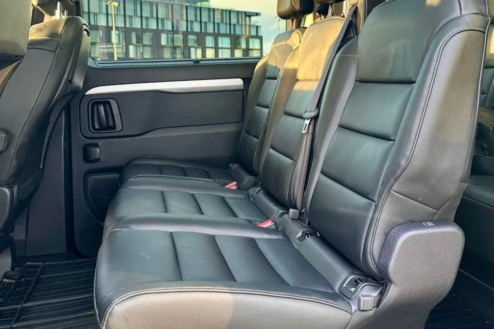 Three black leather car seats in a well-lit vehicle interior, with the door and window visible in the background.