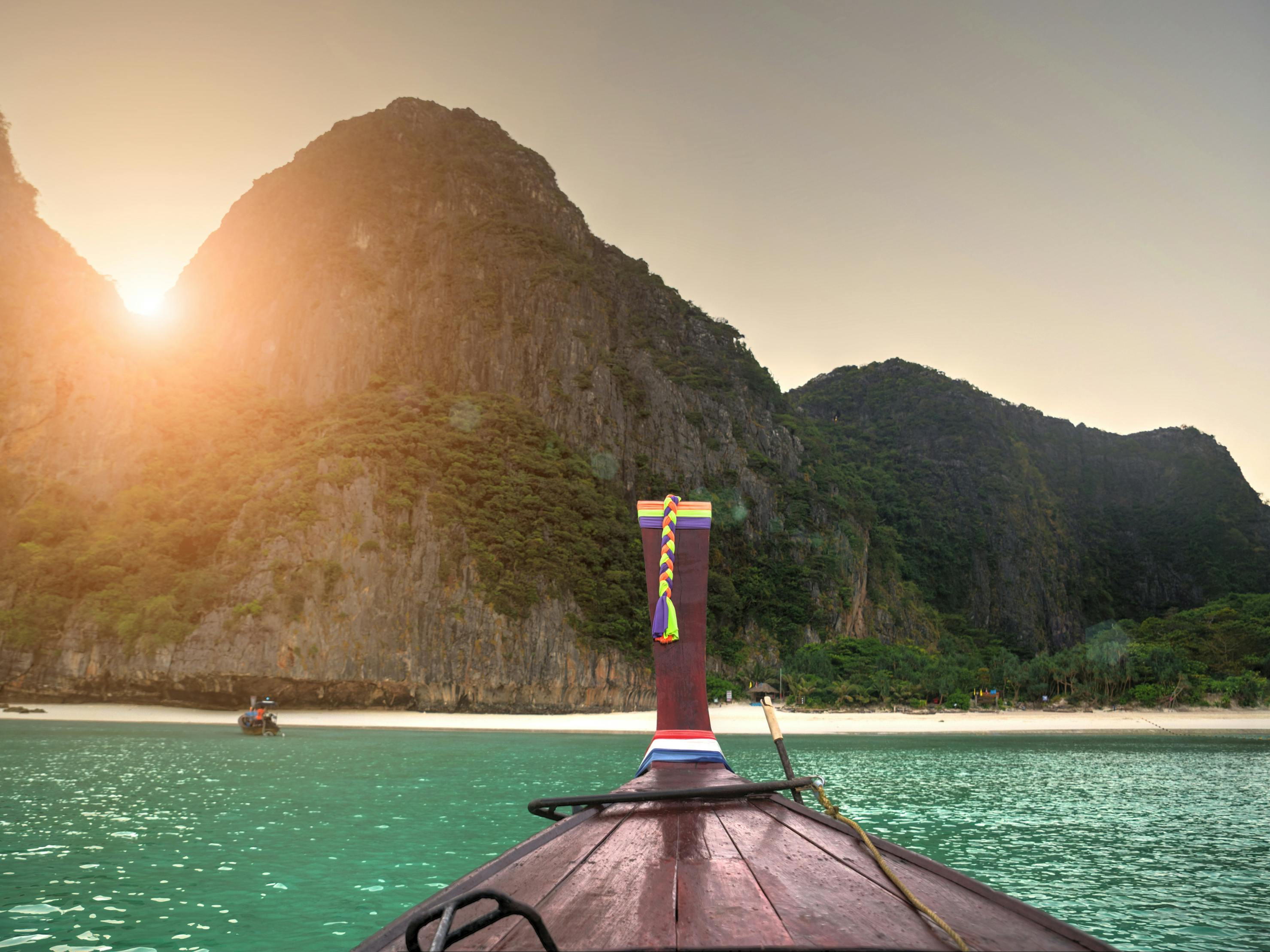 Un bateau à longue queue s'approche d'une plage de sable avec des collines verdoyantes et la lumière du soleil qui illumine la scène.