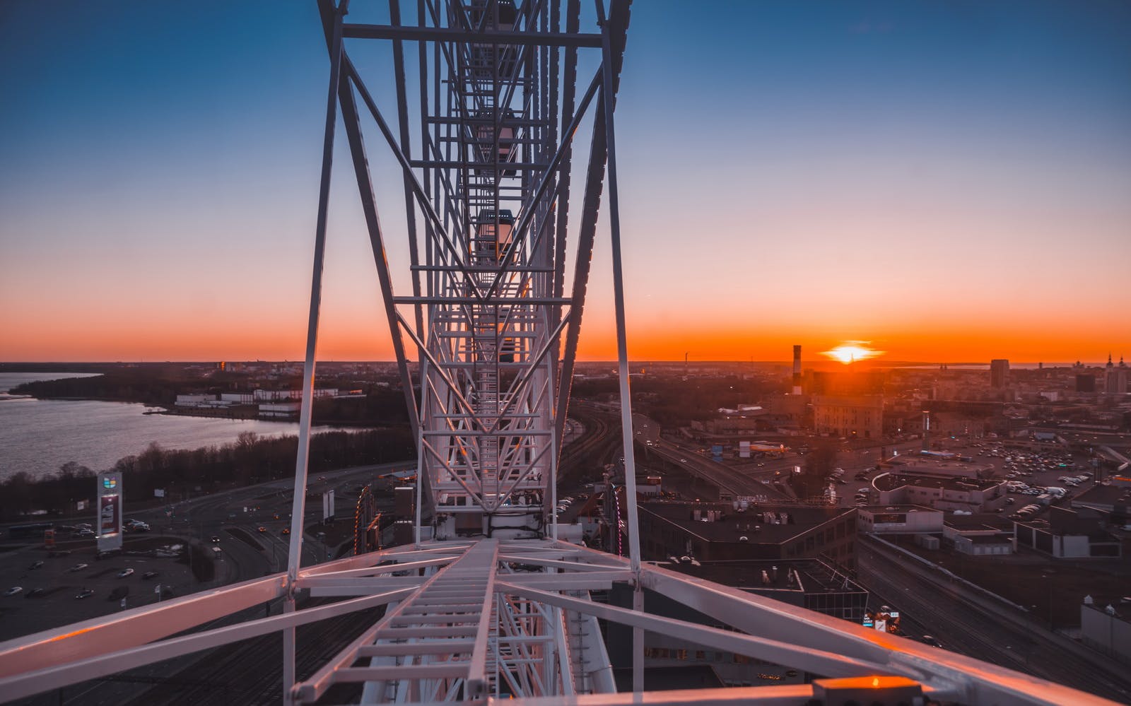View from a Ferris wheel structure at sunset, overlooking roads, buildings, and a distant river.