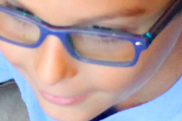 Un ragazzino con gli occhiali e una maglietta blu, che tiene in mano delle palline arancioni mentre gioca su un tappeto con bordi verdi e piccoli giocattoli.