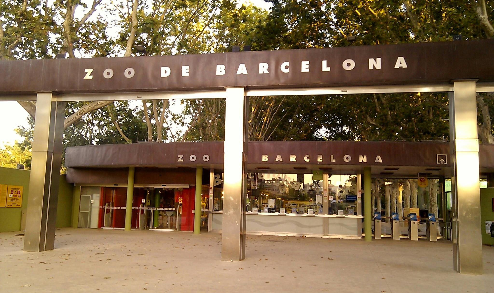 Entrée du Zoo de Barcelone avec des panneaux au-dessus des portes et des arbres en arrière-plan.
