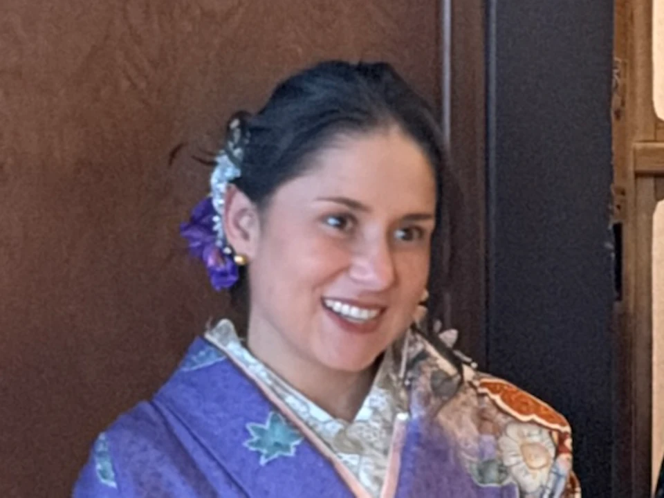 Three people in traditional Japanese attire sit on a tatami mat holding tea bowls while someone photographs them.