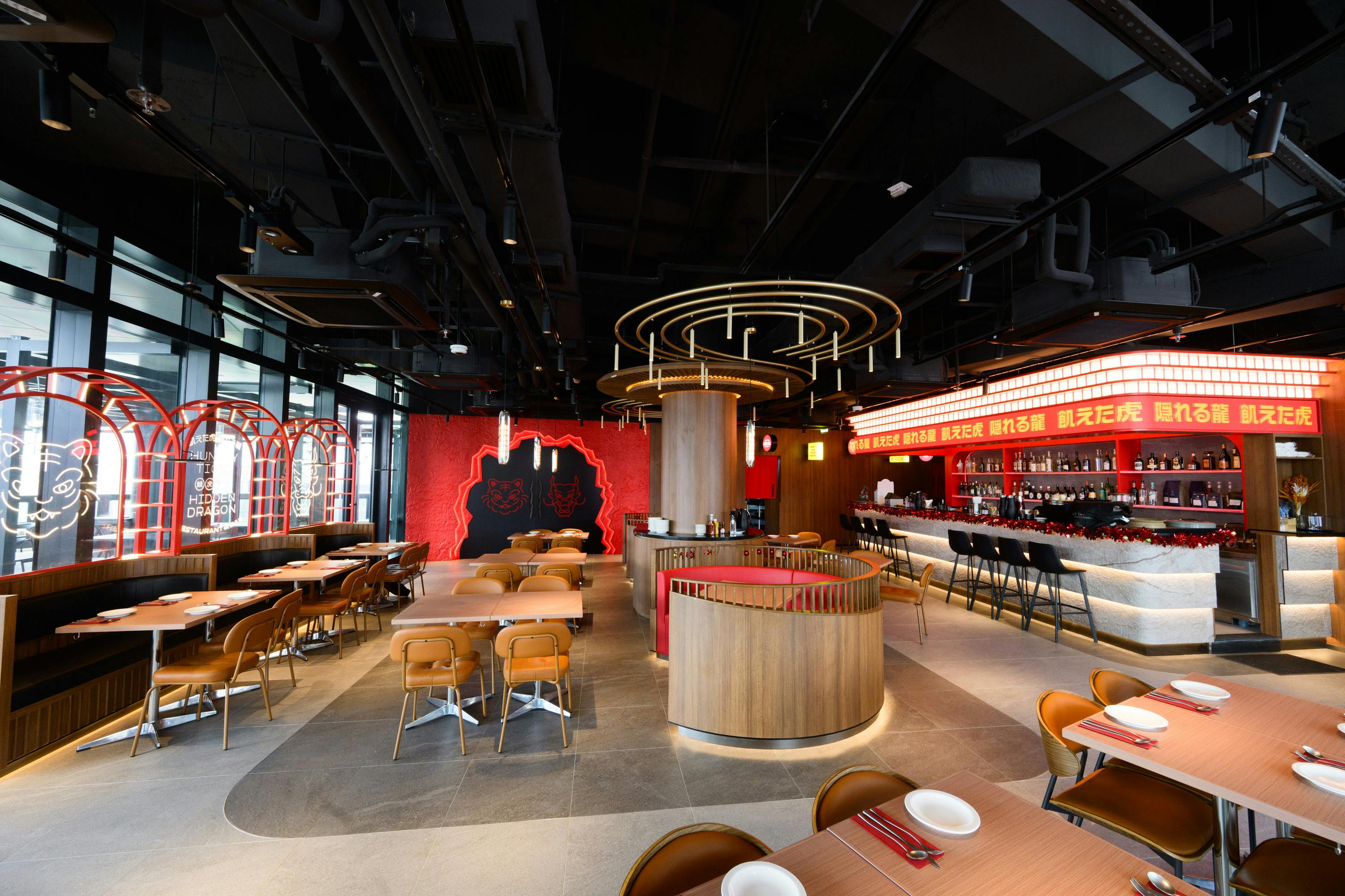 Modern restaurant interior with wooden furniture, red accents, circular counter, and decorative lighting.