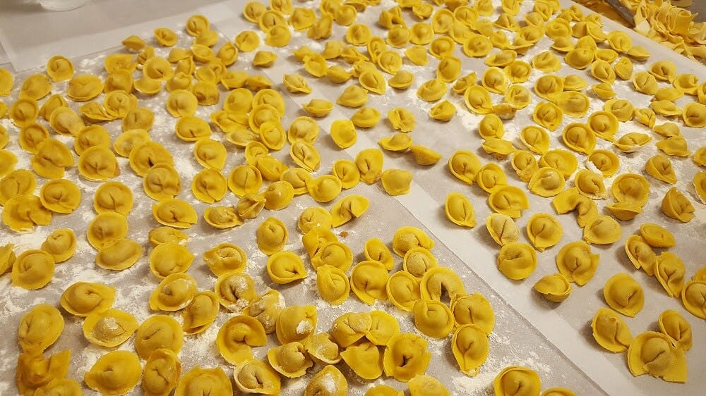 Δεκάδες φρεσκοφτιαγμένα τορτελίνια απλωμένα σε αλευρωμένη λαδόκολλα.