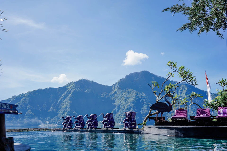 A row of purple elephant statues beside a pool with mountains and a blue sky in the background.