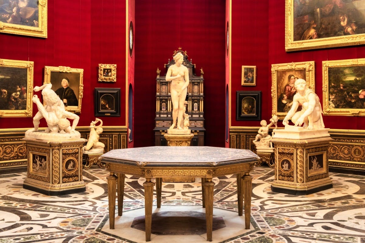 Une pièce aux murs rouges, avec des sculptures classiques, des tableaux encadrés et une grande table octogonale dont le sol est orné de motifs complexes.