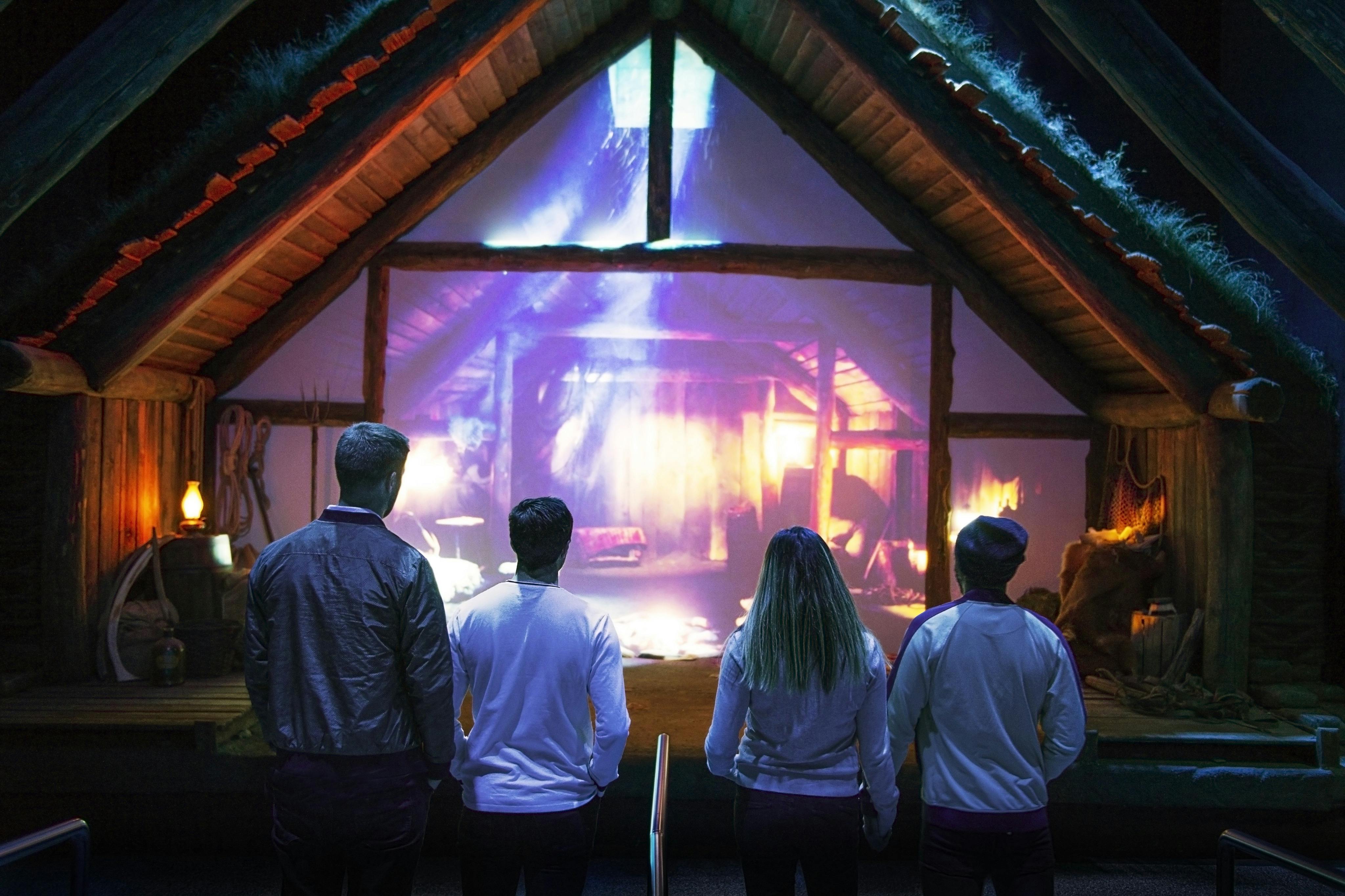 Vier Personen stehen vor einem Fenster, das eine lebendige Szene eines rustikalen Hütteninneren mit lebhaften Lichteffekten zeigt.