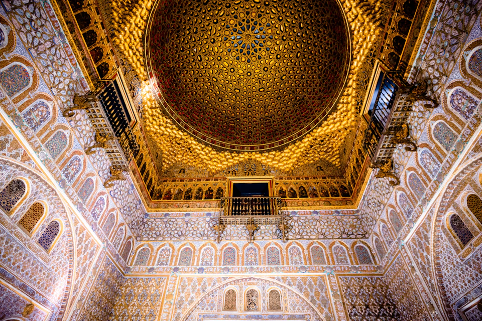 Elaborate, gold-decorated domed ceiling with intricate patterns, arches, and balconies in a richly adorned interior room.