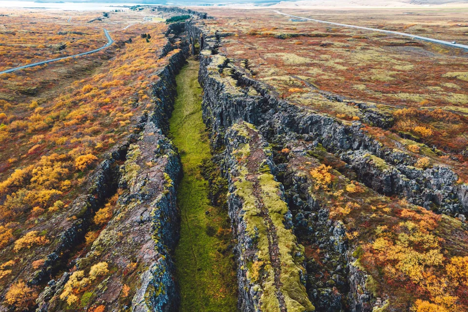 Aerial view of a rocky fissure covered with moss and surrounded by autumn-colored vegetation in a vast landscape.