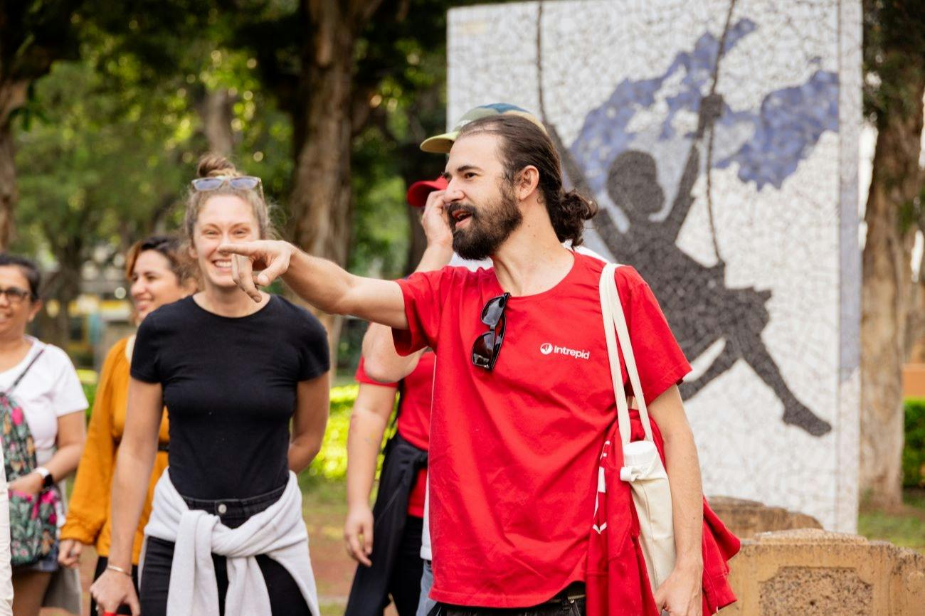 A group of people outdoors, with a man in a red shirt pointing and others smiling in the background.