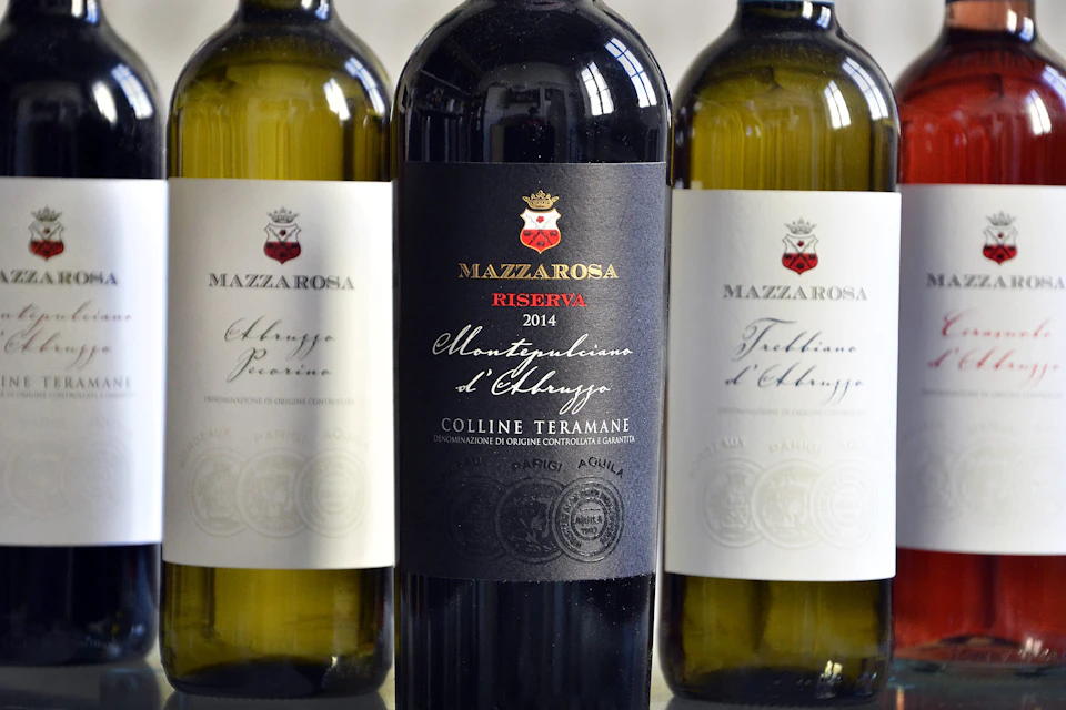 Three wine bottles; the center bottle is a red wine labeled "Mazzarosa Riserva 2014," flanked by two white wines.