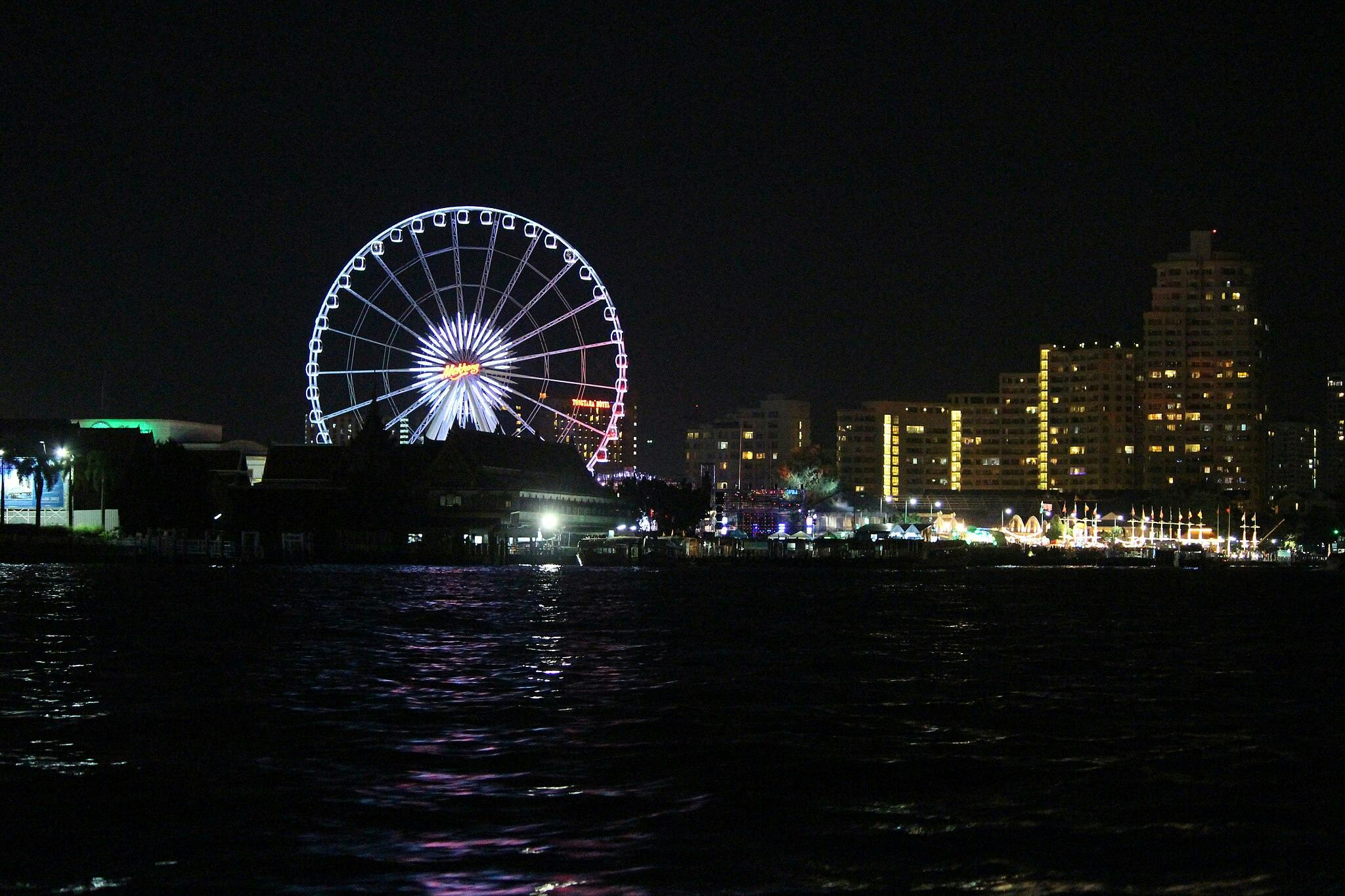 Noční panorama s osvětleným ruským kolem, budovami a nábřežními odlesky.