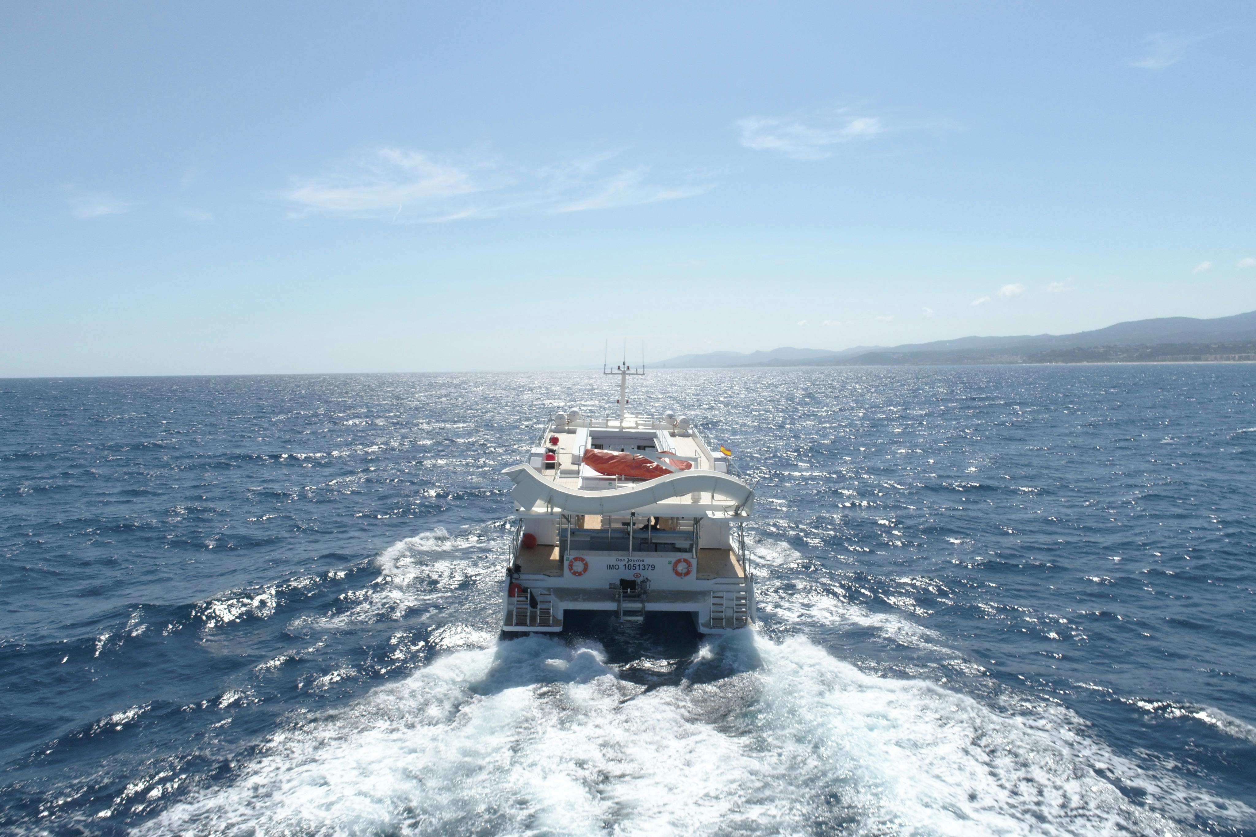 A boat sailing in the ocean with a wake trailing behind it under a clear blue sky.