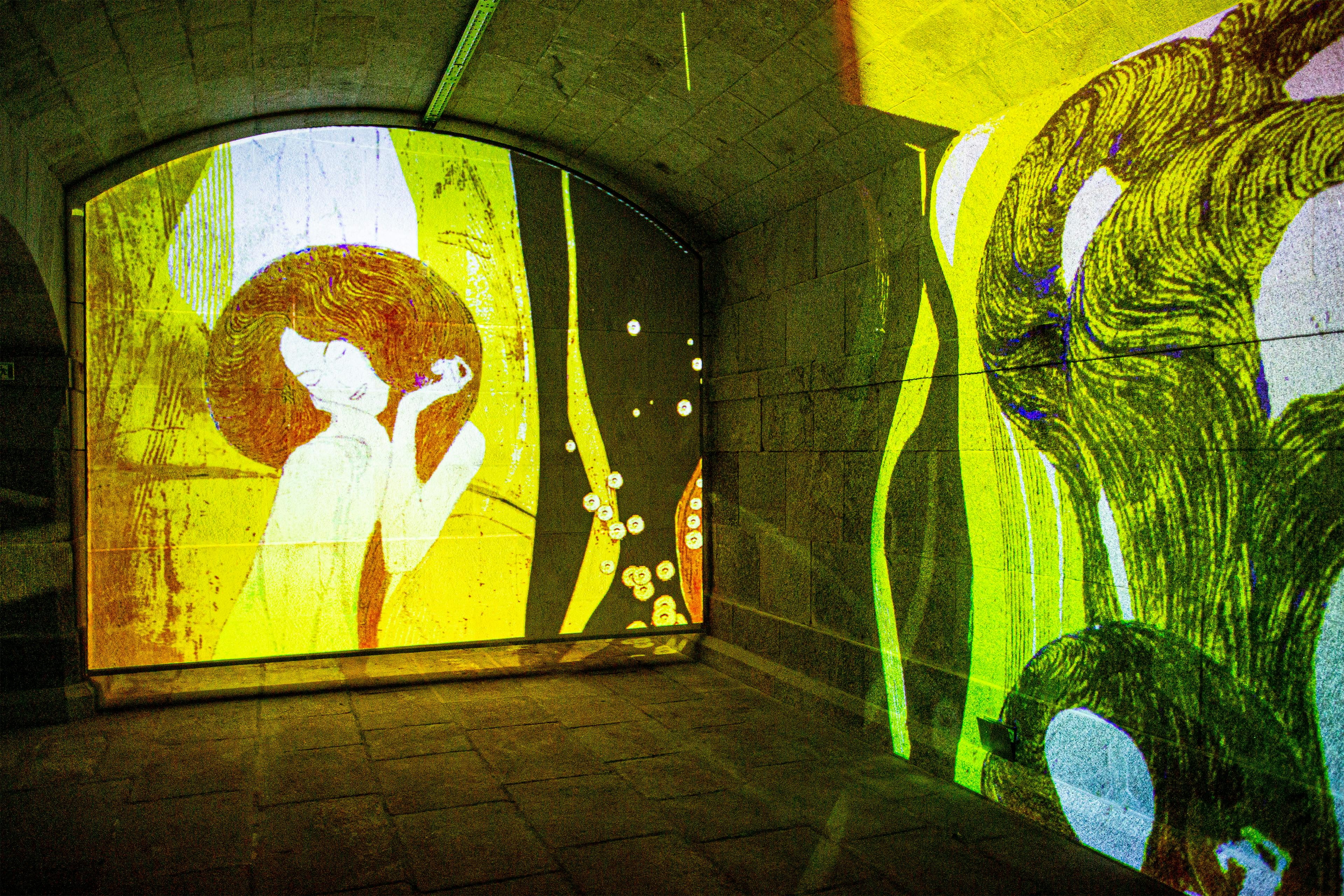 流れるような髪の姿を特徴とし、抽象芸術と花の芸術のカラフルな投影で照らされたアーチ型の石室。