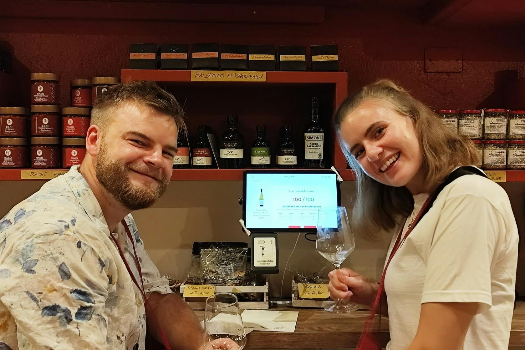 一位身穿花衬衫的男士在吧台前微笑，背景是酒瓶和罐子。