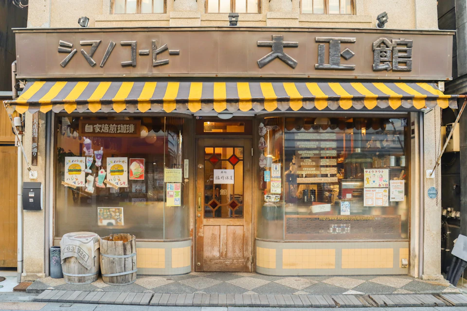 A vintage storefront with a yellow-striped awning, wooden door, and large windows displaying items and posters.