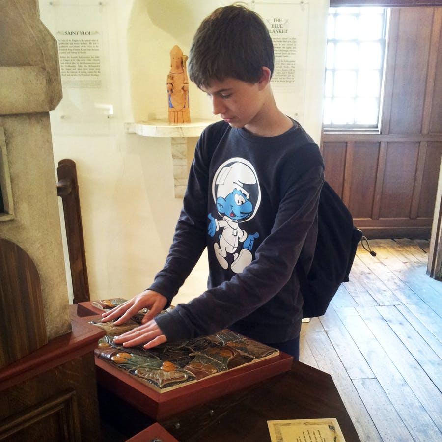 Un bambino che indossa una maglietta dei Puffi e uno zaino interagisce con un'esposizione tattile in un museo.