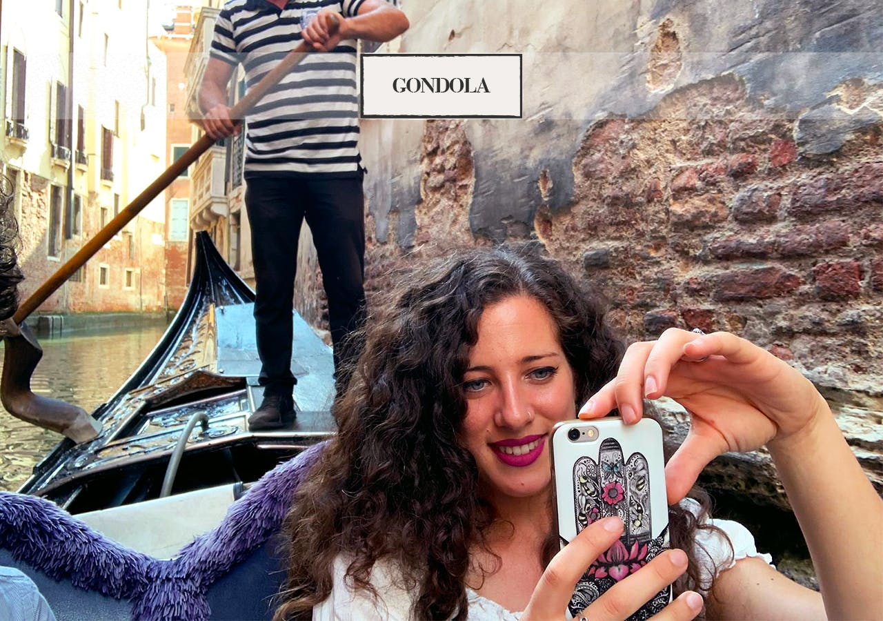 벽돌 벽 앞에 줄무늬 셔츠를 입은 곤돌라를 입은 한 여성이 곤돌라 위에서 셀카를 찍고 있습니다.