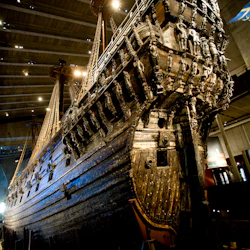 Ett stort, välbevarat träskepp med invecklade sniderier som visas i ett museum, sett underifrån.