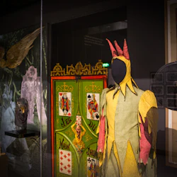 En museivisning med en färgglad skojarkostym, vintage bioutrustning, en dekorerad panel och olika affischer och artefakter.