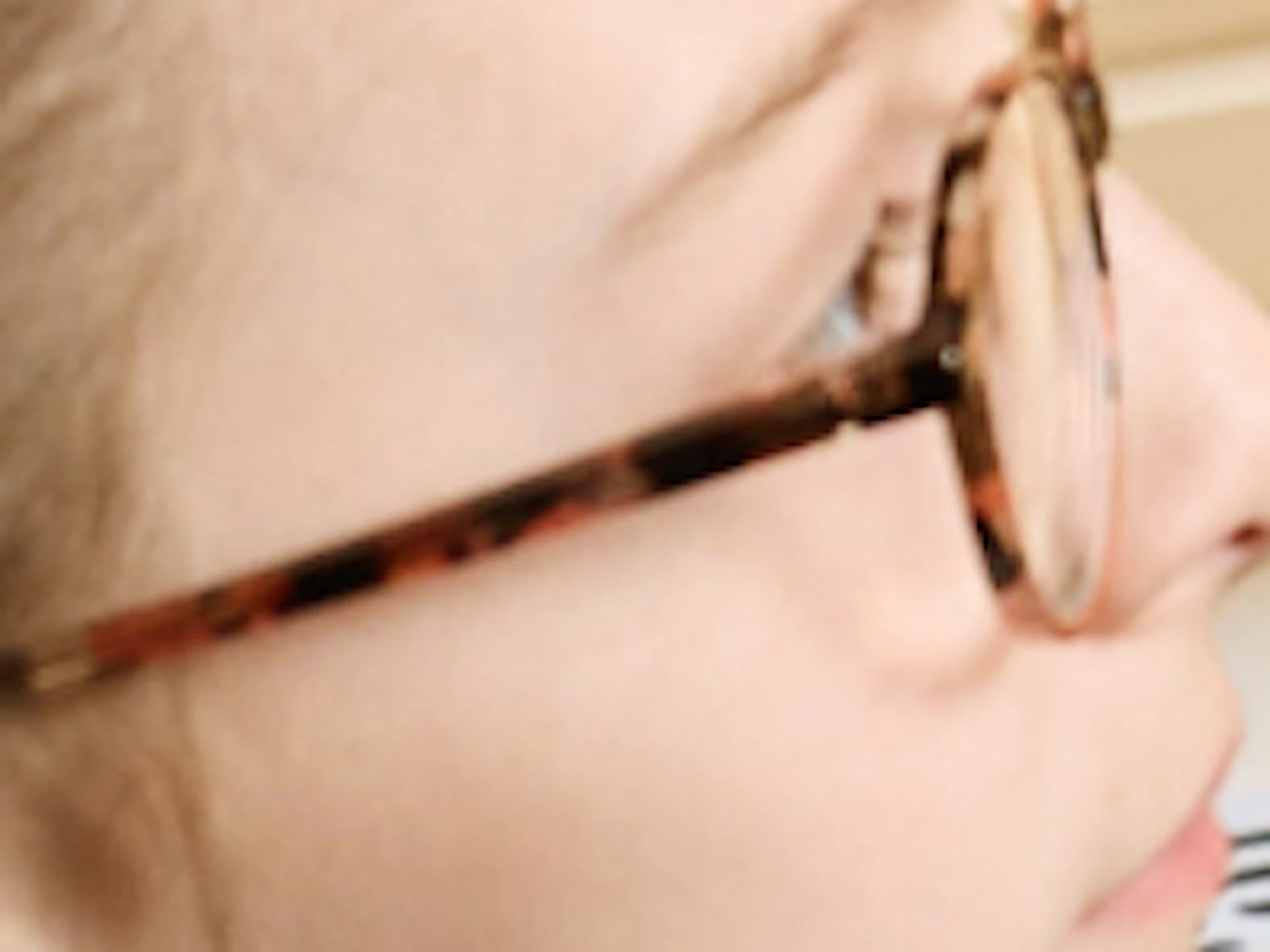 A person with braided hair and glasses looks at a violin on display inside a room with a large window showing an ornate clock.