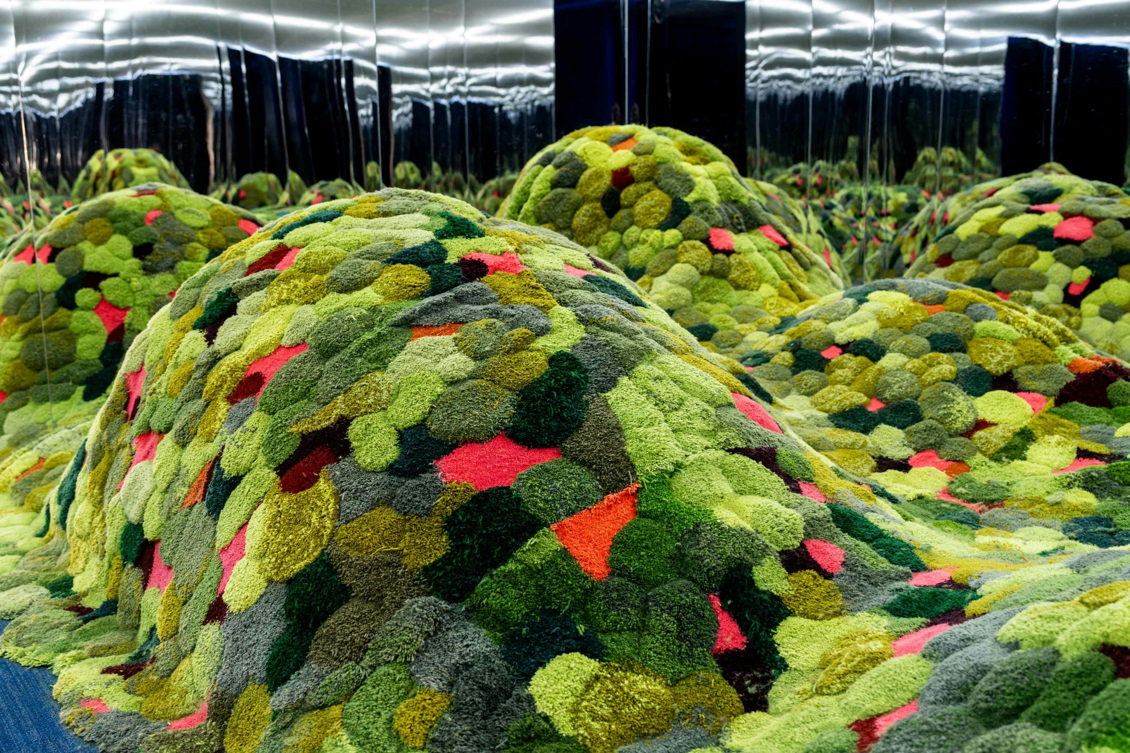 Colorful mounds of plush, textured fabric in an art installation with mirrored walls reflecting the vibrant patterns.