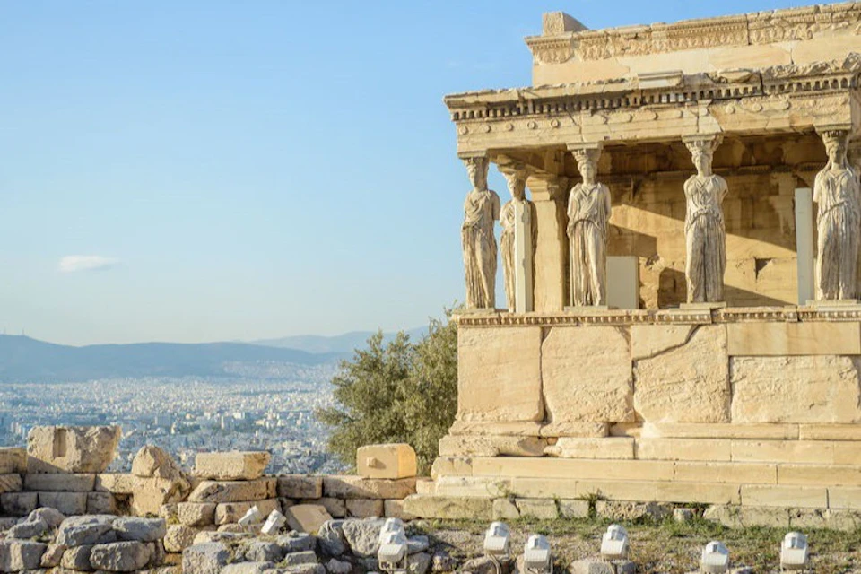 A historic building with statues as columns, overlooking a cityscape under a clear blue sky.
