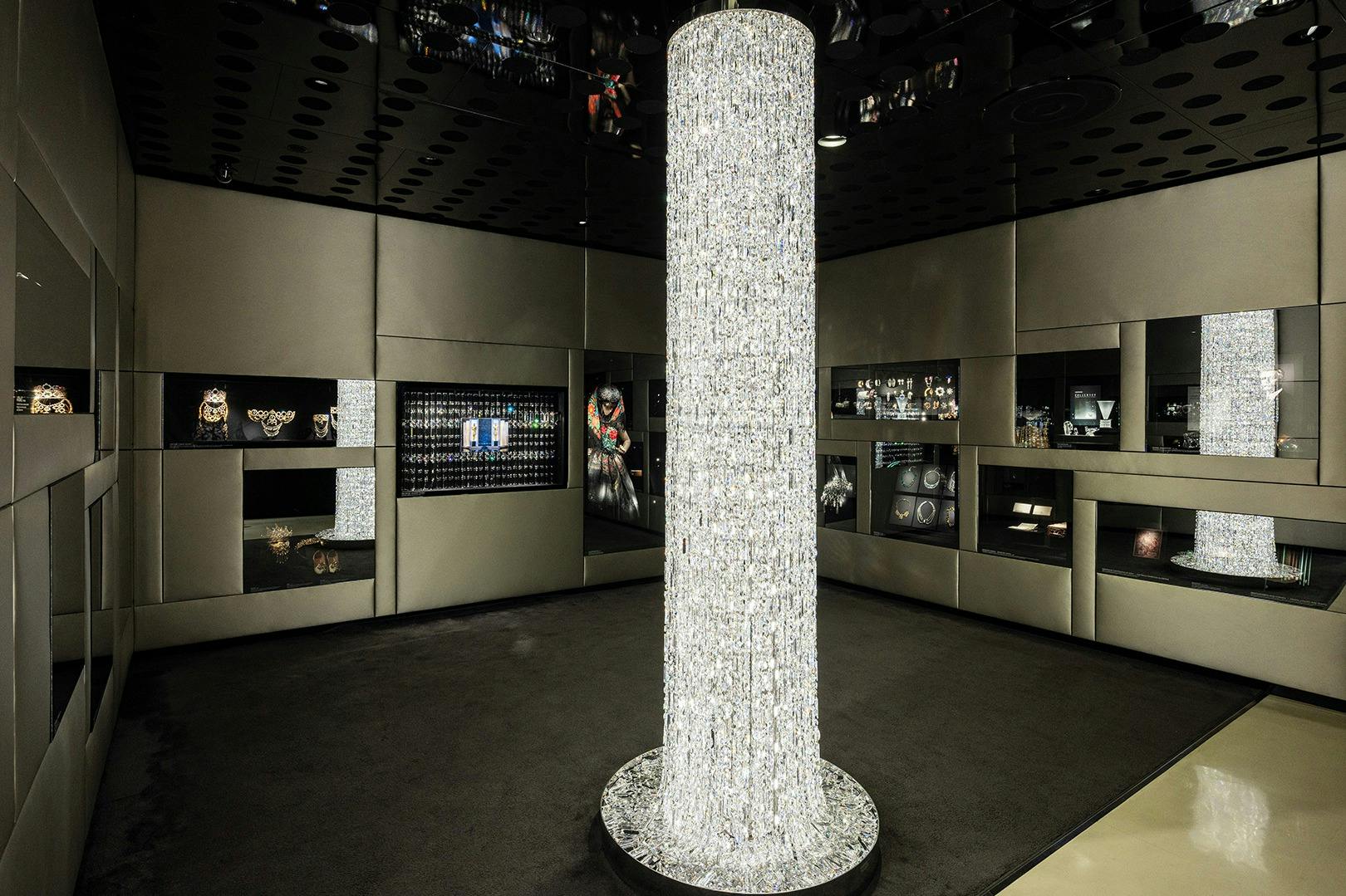 ジュエリーやアクセサリーの陳列ケースに囲まれた、背の高い円筒形のクリスタルシャンデリアを備えた豪華なショールーム。