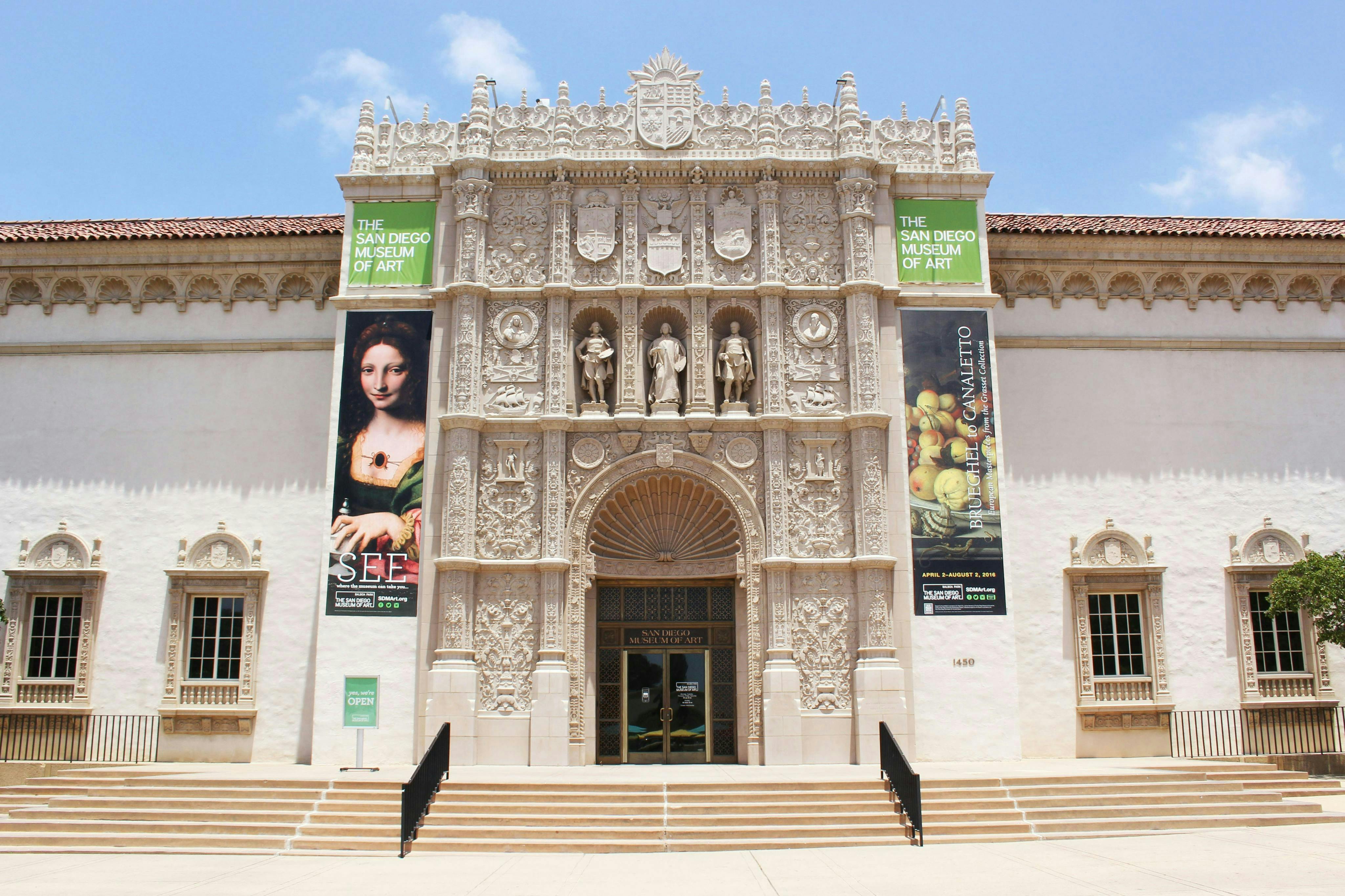 La facciata del San Diego Museum of Art con sculture in pietra decorate, due grandi striscioni con opere d'arte e un ingresso ad arco.