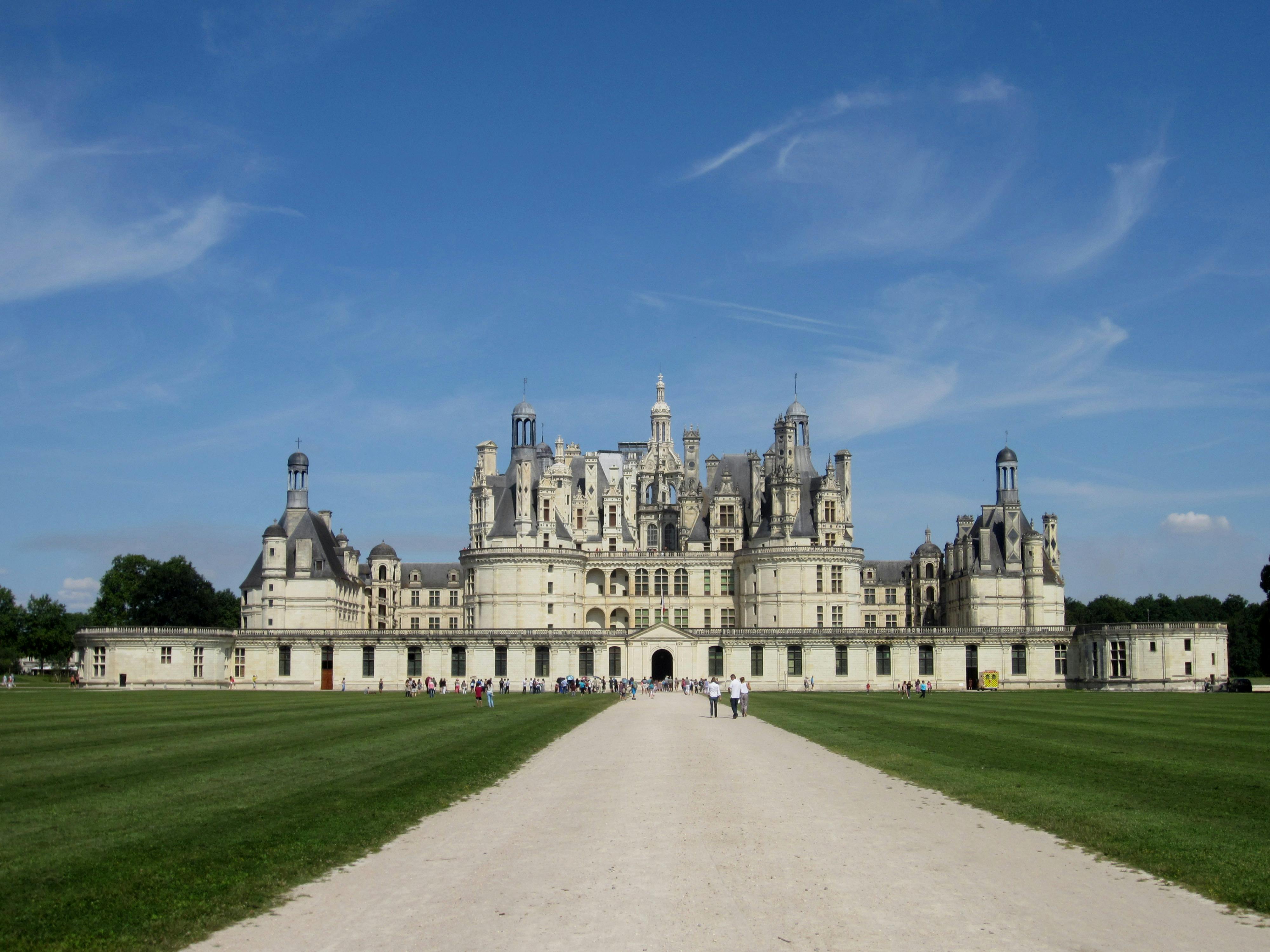 大型历史悠久的城堡，华丽的塔楼，四周环绕着修剪整齐的草坪和宽阔的小径，在晴朗的蓝天下。