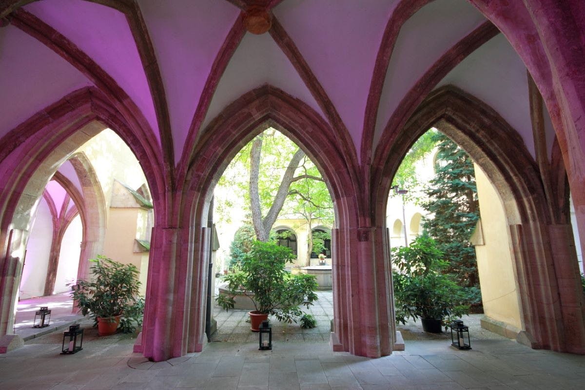 A covered archway with pointed arches opens to a garden courtyard with potted plants, lanterns, and a large tree in the center.