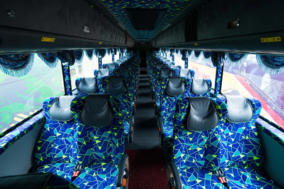 Interior of a bus with rows of blue and green patterned seats and large windows on both sides.