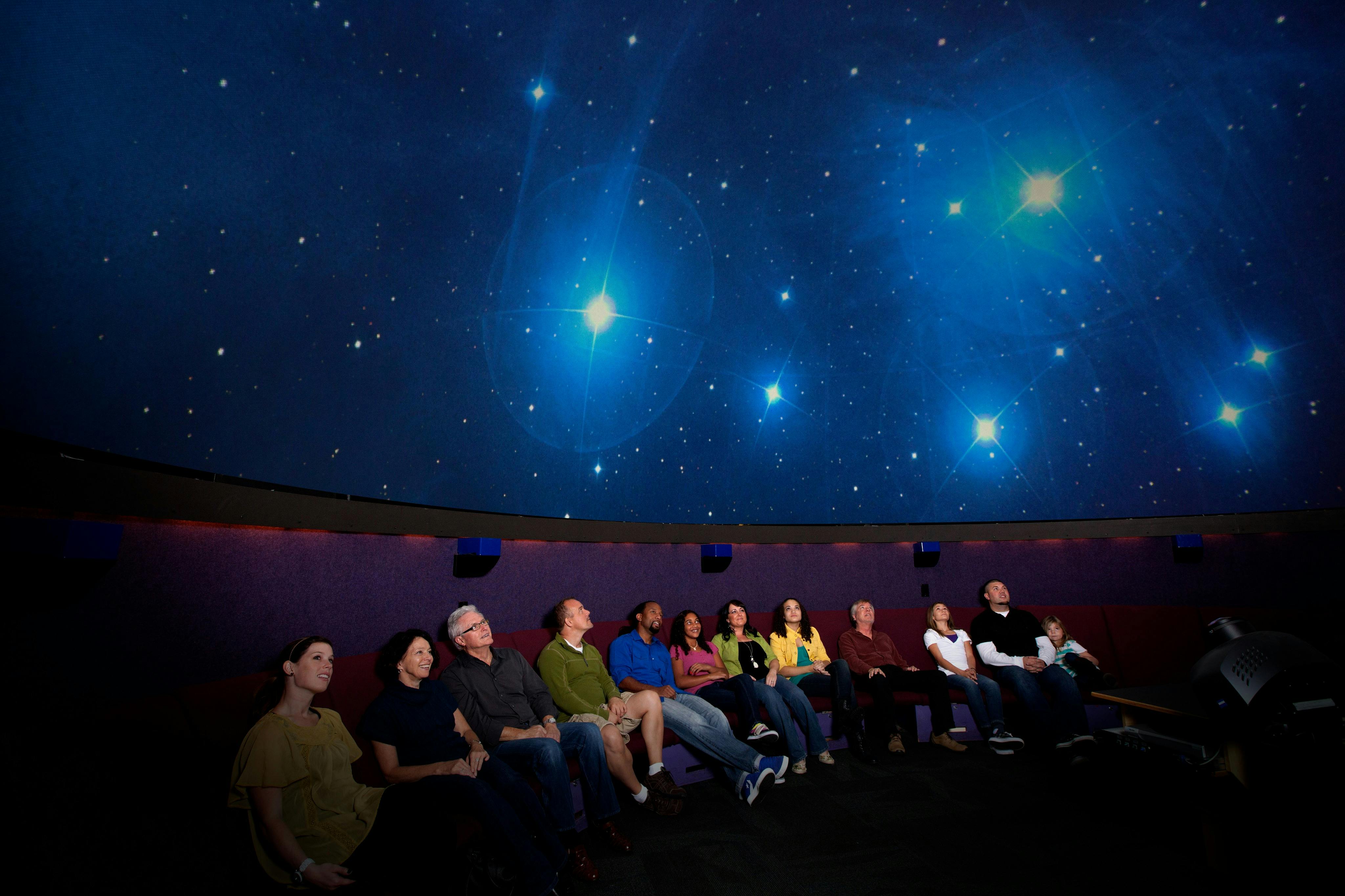 Een groep mensen zit in het Planetarium sterren te kijken aan de nachtelijke hemel.