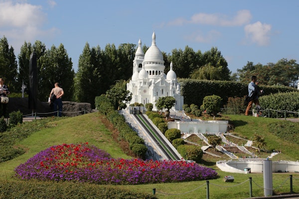 Un detallat model en miniatura d'un edifici amb cúpula blanca envoltat de vegetació i llits de flors de colors, vist en un parc a l'aire lliure.