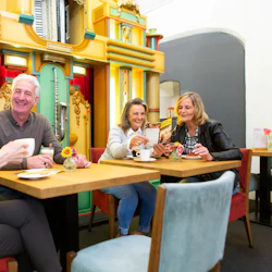 Fyra personer njuter av drinkar och samtal på ett kafé, med en livlig, dekorativ vägg i bakgrunden.