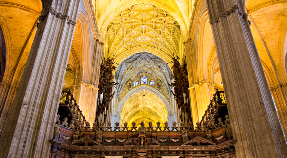 Intricately designed cathedral interior with vaulted ceilings, ornate carvings, and stained glass windows.