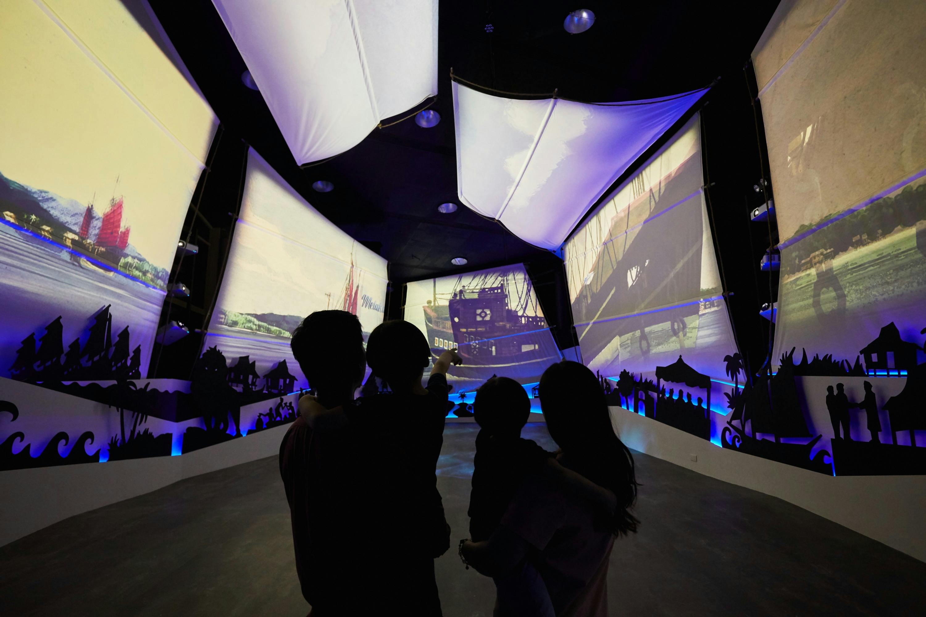 Silhouetted family observing large, illuminated nautical-themed screens in an immersive, dark exhibition space.