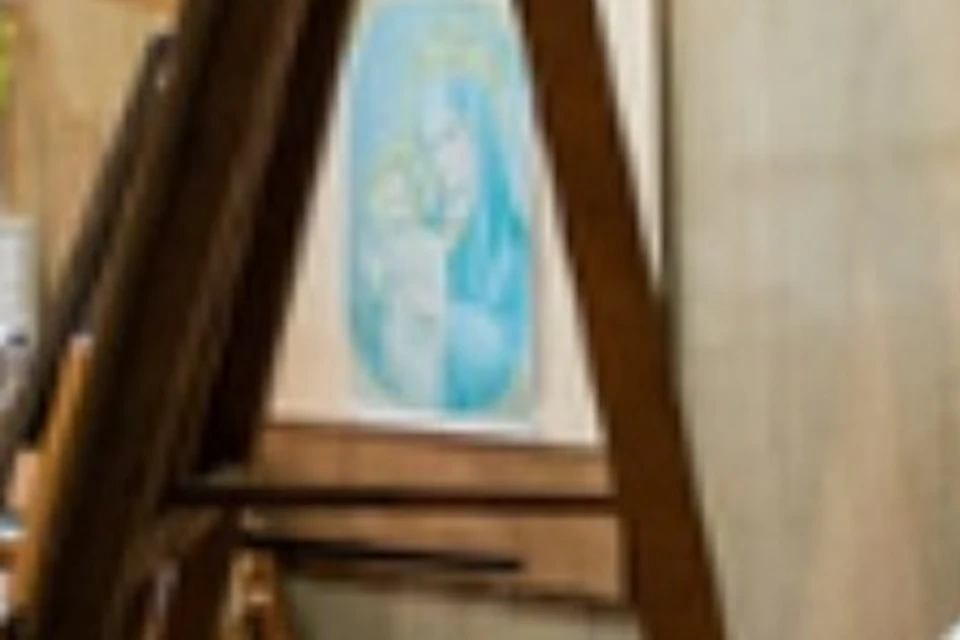 Two artists work on religious paintings in a studio with art supplies and an easel under soft lighting.